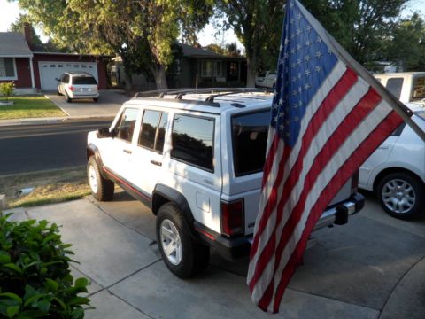 1994 Jeep Cherokee - White 1994 Jeep Cherokee with an American flag mounted on the back, parked in a suburban driveway.
