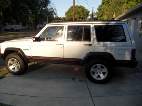 1994 Jeep Cherokee - This white 1994 Jeep Cherokee SUV is seen from the side, parked on a driveway with red pinstripes visible.