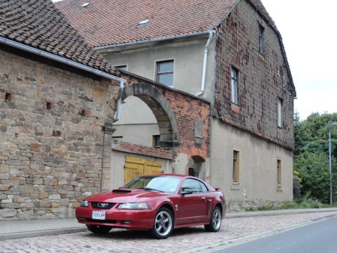 2003 Mercury Marauder - This red 2003 Ford Mustang coupe is parked on a cobblestone street in front of a historic building.
