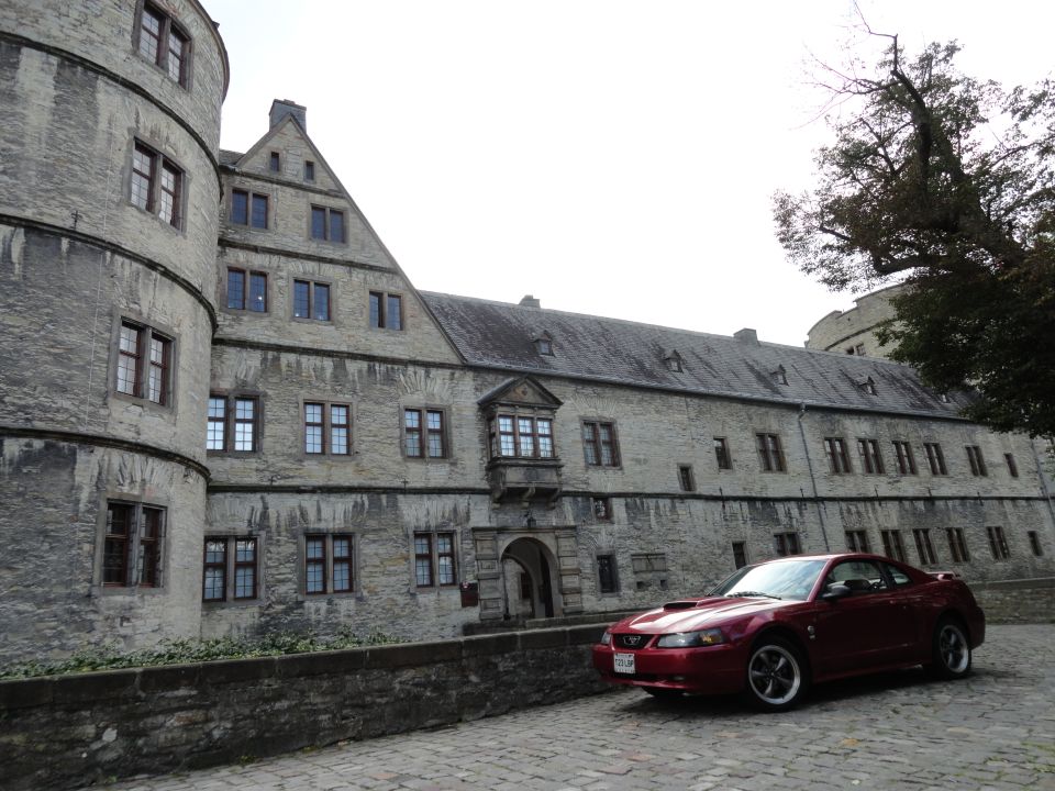 Red coupe with hood scoop parked on cobblestone street