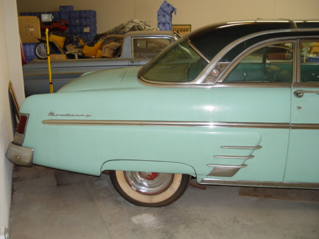 Side rear quarter of turquoise 1954 Mercury Monterey with whitewalls in a garage