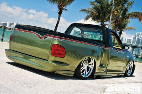 2007 Ford Mustang - This modified pickup truck features a unique green paint job and aggressive stance, set against a coastal urban backdrop.