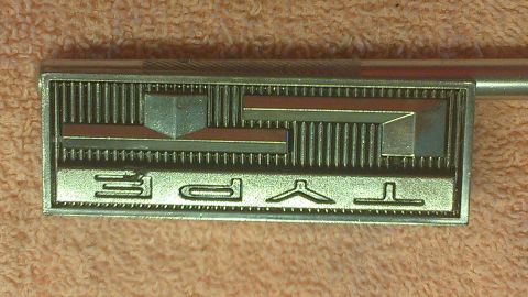 1973 Chevrolet Camaro - A chrome emblem with red accents and raised geometric shapes is shown close-up.
