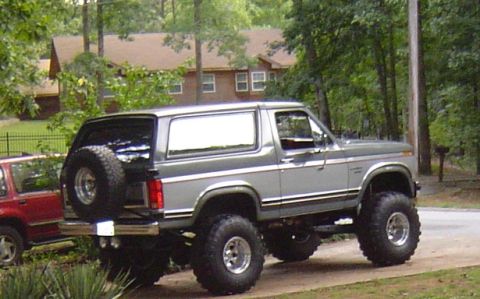 1986 Ford Bronco - This lifted 1986 Ford Bronco is shown in a three-quarter front view, parked next to a red SUV.