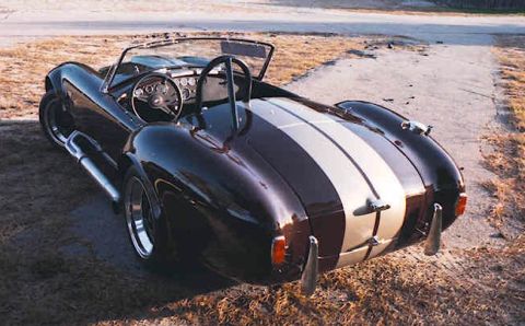 1967 Ford 427 - Rear three-quarter view of a dark purple convertible sports car with white racing stripes.