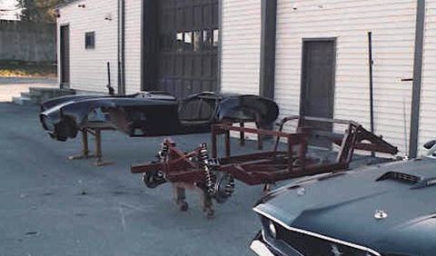 1967 Ford 427 - Two car bodies and a chassis are visible in front of a building, with a partially visible car in the foreground.
