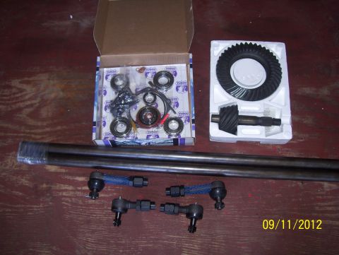 1990 Ford Bronco - Automotive parts including a differential ring gear, pinion gear, axle shaft, and tie rod ends are laid out on a wooden surface.