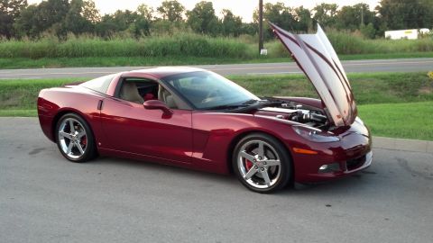 2007 Ford Mustang - A red sports car is parked on the side of the road with its hood open, revealing the engine.
