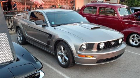 2007 Ford Mustang - A silver Ford Mustang is parked at an outdoor event, with a vintage red car visible to its right.
