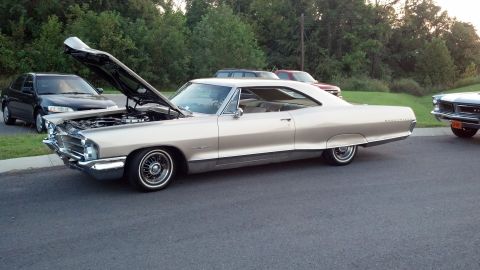 2007 Ford Mustang - A tan 1965 Pontiac Catalina coupe is parked with its hood open, alongside other vehicles.