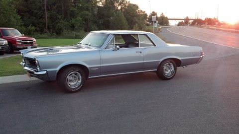 2007 Ford Mustang - A light blue 1965 Pontiac GTO coupe is parked on the side of a road during sunset, with two trucks visible in the background.
