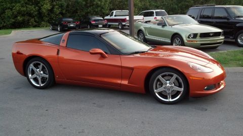 2007 Ford Mustang - An orange Chevrolet Corvette is parked in a lot with other vehicles visible in the background.