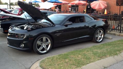 2007 Ford Mustang - A black Chevrolet Camaro is parked outside a building with its hood open, showing the engine.