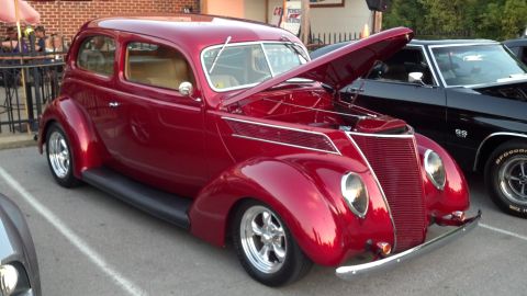 2007 Ford Mustang - A classic red hot rod sedan is parked next to a black muscle car, both with hoods open.