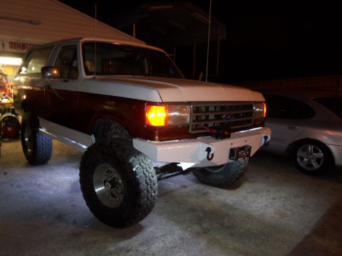 1989 Ford Bronco - This lifted Ford Bronco features a custom front bumper with a winch and tow hooks, parked next to another vehicle.
