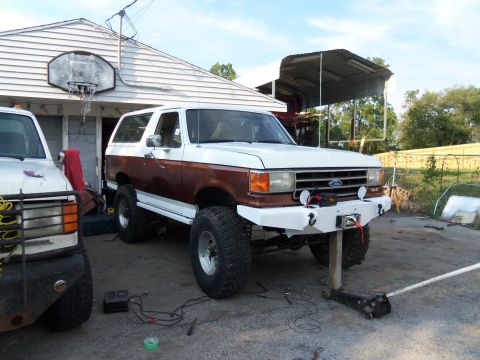 1989 Ford Bronco - A lifted Ford Bronco with a custom bumper sits in a driveway next to another vehicle.