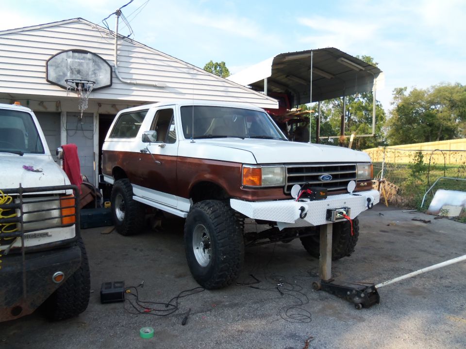 White and brown Ford Bronco with aftermarket bumper and winch, jacked up