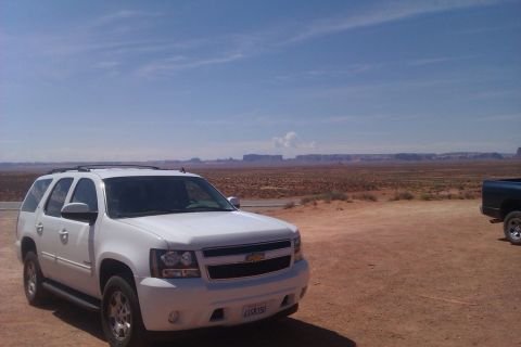 1991 Ford LTD Crown Victoria - White Chevrolet Tahoe SUV parked in Monument Valley with a dark pickup truck in the background.