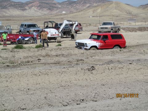 1979 Ford Bronco - A red and white Ford Bronco is stuck in the mud, surrounded by other vehicles and people on a dry, dusty landscape.