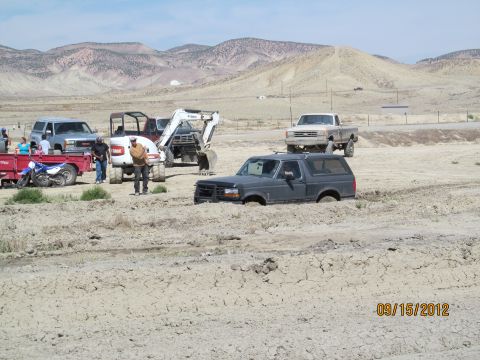 1979 Ford Bronco - A dark gray Ford Bronco is stuck in mud with other vehicles and construction equipment nearby.