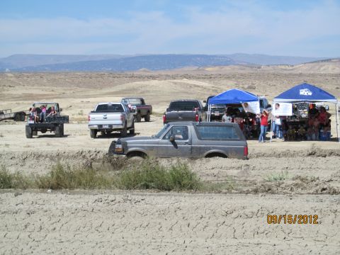 1979 Ford Bronco - Several vehicles are present at a muddy outdoor event, with one SUV deeply stuck in the mire.