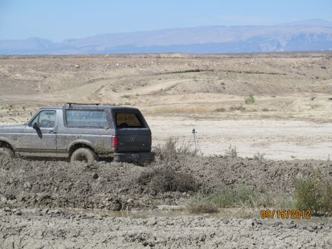1979 Ford Bronco - A Ford Bronco is stuck in thick mud on a dry, dusty terrain with mountains in the distance.