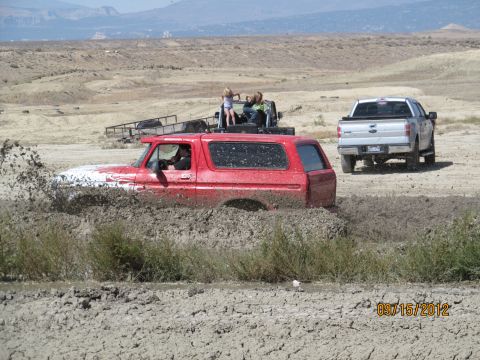 1979 Ford Bronco - A red SUV is stuck in a mud pit, with a silver pickup truck nearby.