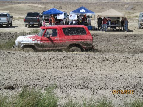 1979 Ford Bronco - A red 1979 Ford Bronco navigates a muddy track during an event, with spectators and other vehicles present.