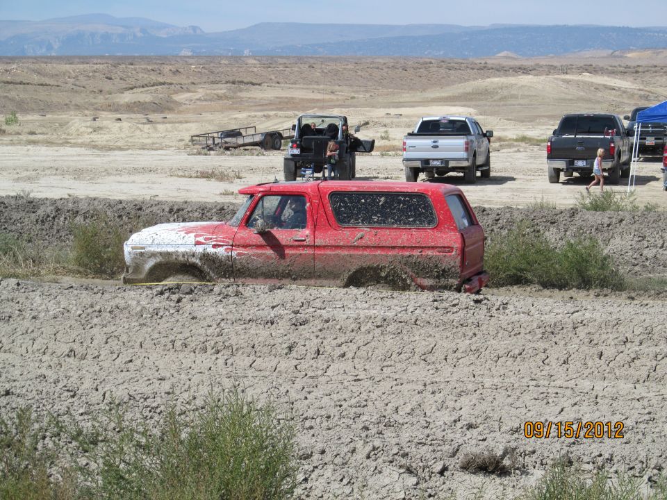 Red SUV stuck in mud, front half submerged, white paint on hood