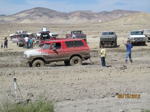 1979 Ford Bronco - Several vehicles are gathered in a muddy, outdoor area, with one red Bronco deeply stuck in the mire.