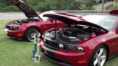 2007 Ford Mustang - Two red Ford Mustangs are displayed with their hoods open, accompanied by trophies on a grassy field.