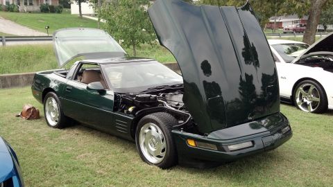2007 Ford Mustang - A dark green Chevrolet Corvette is parked on grass with its hood and rear hatch open, revealing the engine and interior.