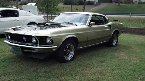 2007 Ford Mustang - Gold 1969 Ford Mustang coupe with black accents parked on grass beside a white modern Mustang.