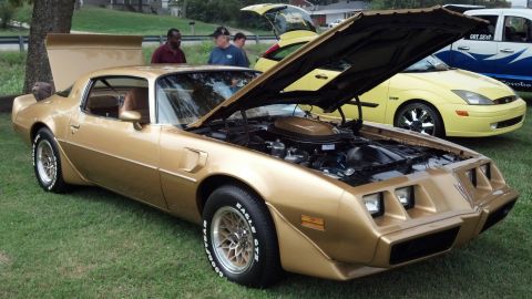 2007 Ford Mustang - Gold 1977 Pontiac Firebird Trans Am on display with its hood open.
