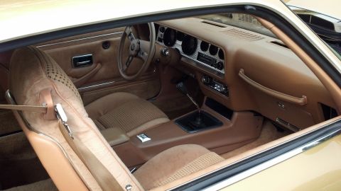 2007 Ford Mustang - The interior of a 1977 Pontiac Firebird features a tan color scheme with patterned seat inserts and a wood-grain-look dashboard.
