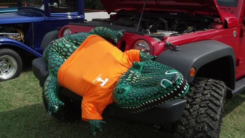 2007 Ford Mustang - An inflatable dinosaur is draped over the front of a red Jeep at an outdoor car show.