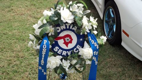 2007 Ford Mustang - A wreath with a Pontiac logo and 'RIP' ribbon is placed next to a white car, possibly a memorial.