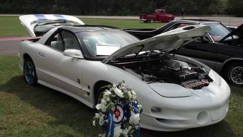2007 Ford Mustang - A white Pontiac Firebird is displayed with its hood and trunk open, alongside other vehicles at an outdoor car show.