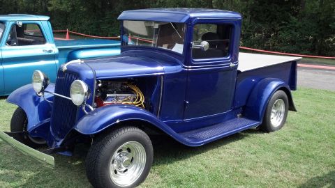 2007 Ford Mustang - A custom blue pickup truck with an exposed engine is parked on grass next to another truck.