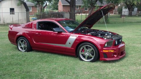 2007 Ford Mustang - A red 2007 Ford Mustang is parked on a grassy lawn with its hood open, revealing the engine compartment.