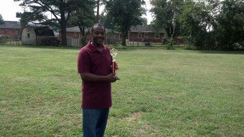 2007 Ford Mustang - A man stands in a field holding a trophy, with houses and trees visible behind him.