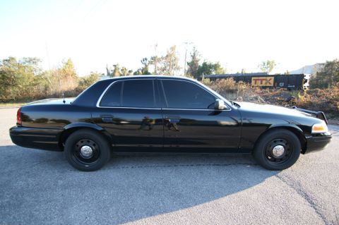 2004 Ford Crown Victoria - Side profile of a black 2004 Ford Crown Victoria sedan with tinted windows and a push bar.