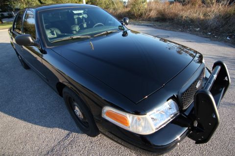 2004 Ford Crown Victoria - This black 2004 Ford Crown Victoria police car is viewed from the front three-quarter angle, showing its push bar and spotlight.