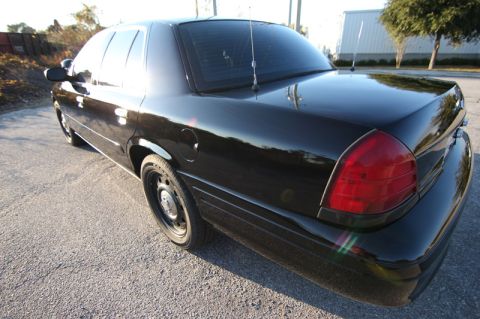 2004 Ford Crown Victoria - A black sedan is parked on a paved surface with trees and a building in the background.