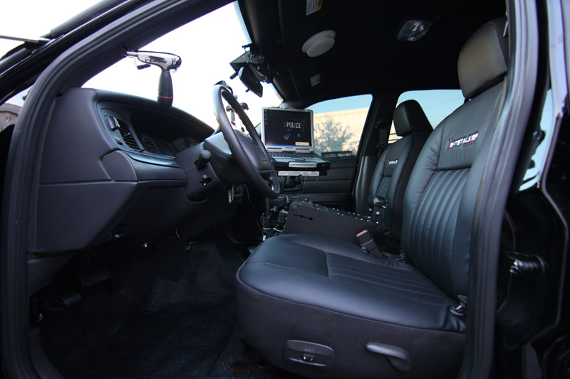 Black leather police car interior with laptop displaying "POLICE", steering wheel, and shotgun mount