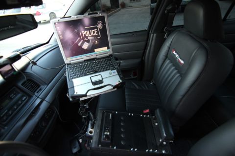 2004 Ford Crown Victoria - The interior of a police vehicle is shown, a mounted laptop displaying a police emblem and the word "POLICE".