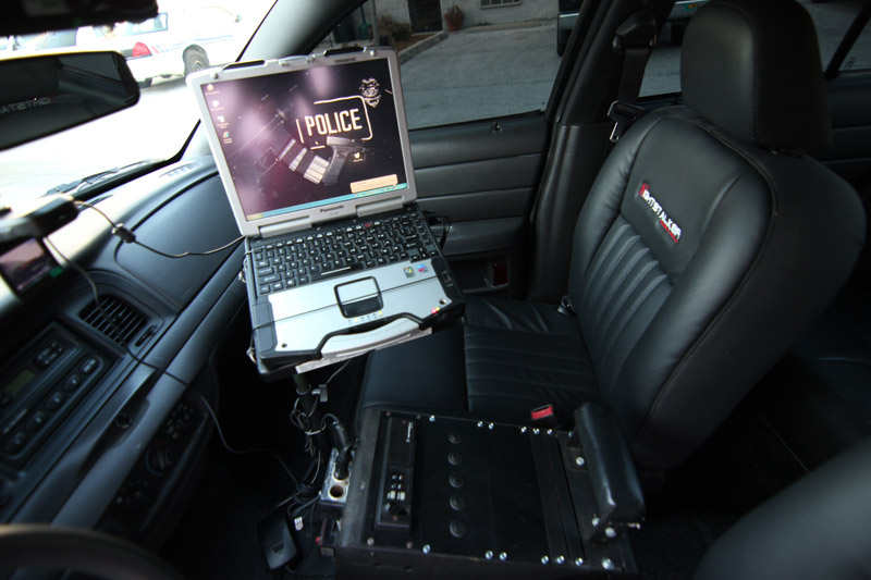 Interior of a police car showing a laptop mounted on the passenger seat, with the word "POLICE" on the screen