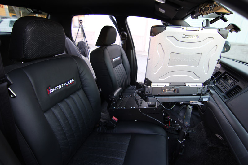 Interior view of a 2004 Ford Crown Victoria police car showing front seats, dashboard, and a Panasonic laptop mounted between the seats