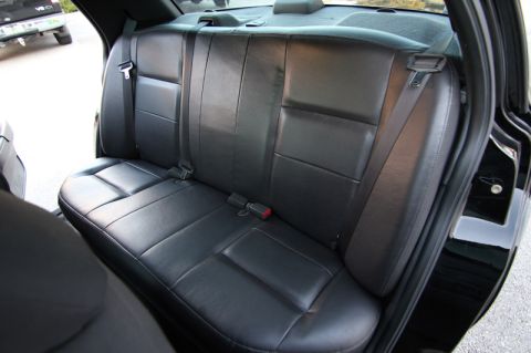 2004 Ford Crown Victoria - Interior view of black leather rear seats in a car, with another vehicle visible through the open door.