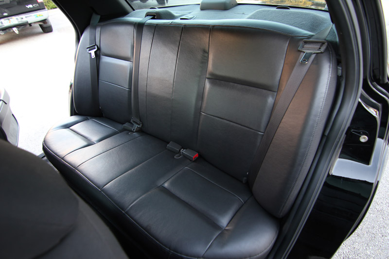 Black leather rear seats with seatbelts inside a car, with a truck visible outside